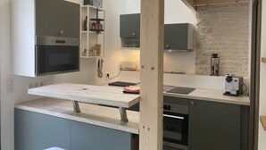 A modern kitchen with built-in appliances, a wooden beam ceiling, and a stone accent wall. - Le Refuge des Bateliers (Arçais)