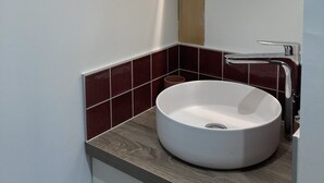 A modern bathroom with a round mirror, a white sink, and a wooden countertop. - Le Refuge des Bateliers (Arçais)
