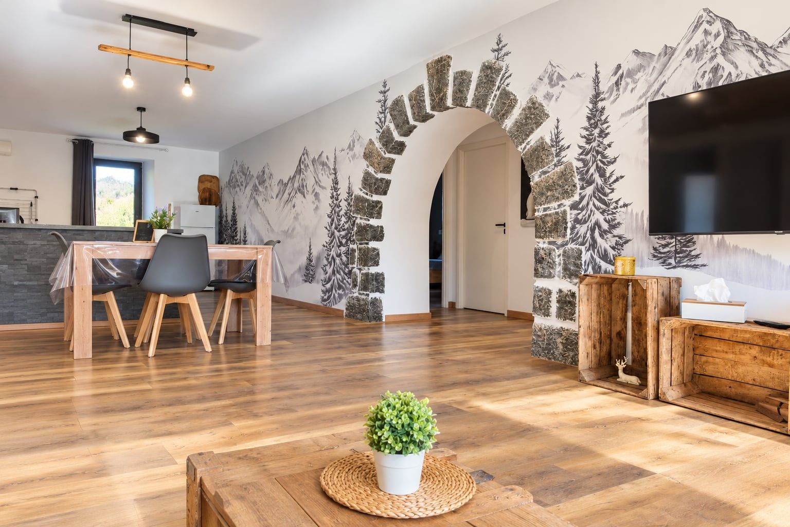 Una sala de estar moderna con una mesa de comedor de madera, sillas, un televisor y un mural de montañas.