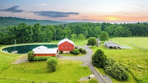 A red barn with a white roof, surrounded by lush green fields and a body of water. - A luxury farm stay with something special for everyone in your group! (Ickesburg)