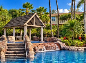 A pool with a waterfall feature, surrounded by rocks and palm trees.