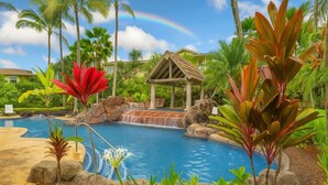 A pool area with a waterfall, surrounded by tropical plants and palm trees.