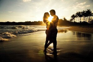 Ein Paar umarmt am Strand, im Hintergrund Palmen und das Meer.