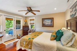 A bedroom with a bed, a ceiling fan, a window with blinds, a chair, and a door leading to an outdoor area.