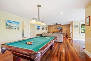 A pool table in a room with wooden flooring, a stone wall, and a ceiling fan.