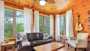L’intérieur chaleureux d’un chalet avec un canapé en cuir, une table basse en bois, un fauteuil blanc et une guitare accrochée au mur.