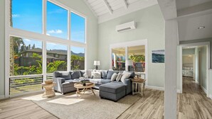 A spacious living room with a large gray sectional sofa, a round coffee table, and a view of lush greenery outside. - Princeville Home w/Private Pool and Mountain View (Princeville)