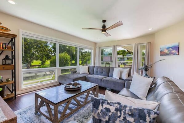 A spacious living room with a large window, a ceiling fan, and a sofa with cushions.