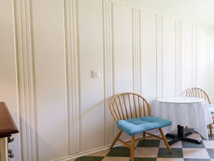 Une pièce avec un sol à carreaux, une table ronde, deux chaises et un buffet en bois.