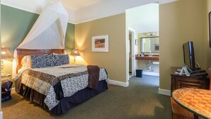 Ein Schlafzimmer mit einem Himmelsbett, Nachttischlampen, einem gerahmten Bild an der Wand und einem Fernseher auf einem Holzständer.