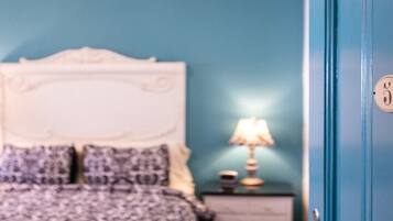 Un dormitorio con una cama, almohadas, una mesita de noche, una lámpara y una puerta con cerradura.