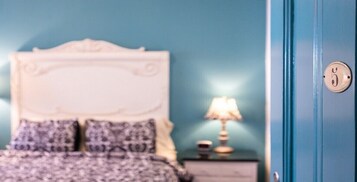 Un dormitorio con una cama, almohadas, una mesita de noche, una lámpara y una puerta con cerradura.