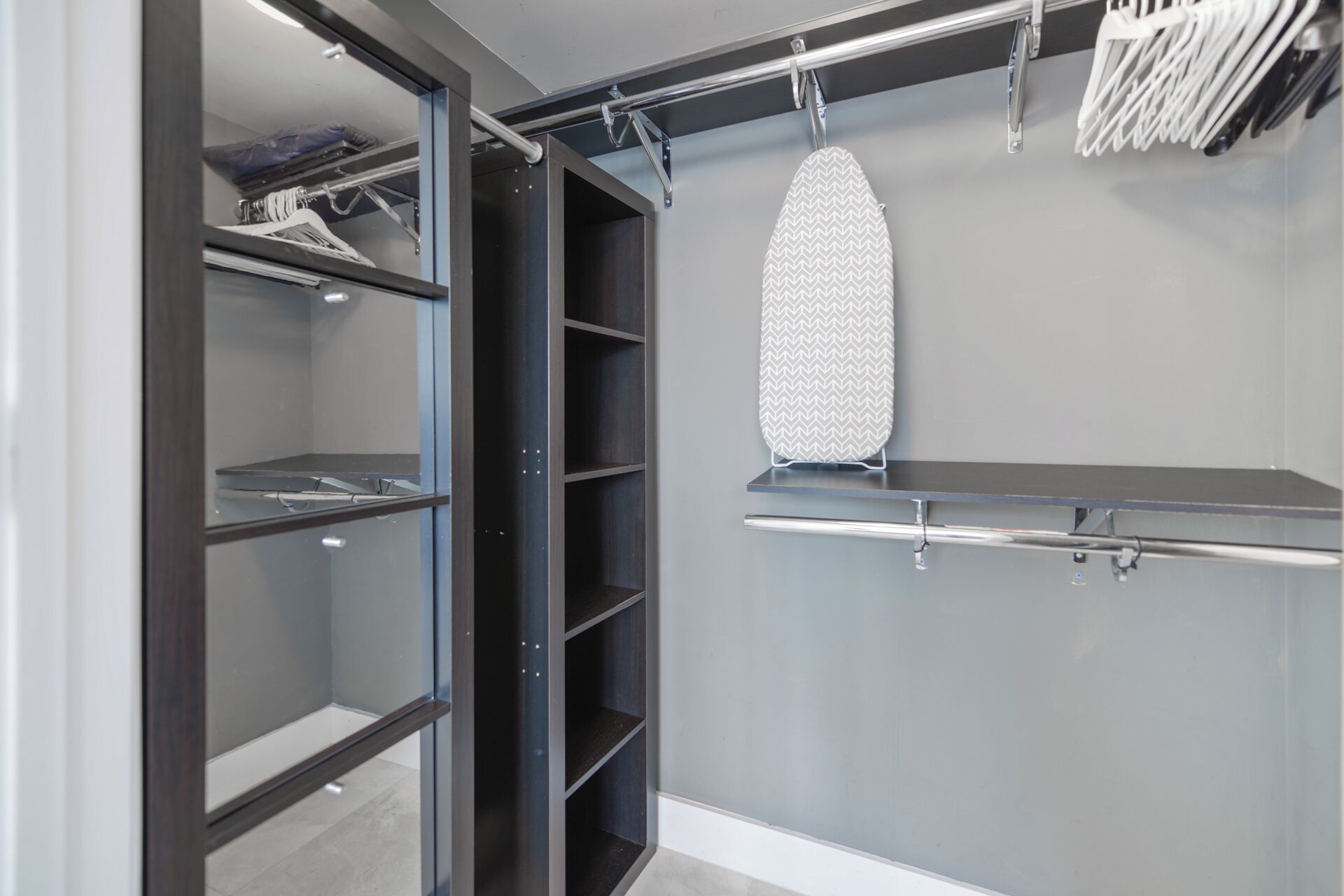 A walk-in closet with open shelves, a hanging rack, and an ironing board.
