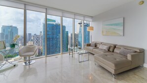 Ein geräumiges Wohnzimmer mit großem Fenster und Blick auf die Stadt, einem beigen Sofa und einem Glastisch.