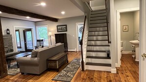 A spacious living room with a wooden floor, a gray sofa, a wooden bench, and a staircase. - 5 minutes to Cooperstown Village - New Renovation! (Cooperstown)