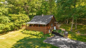 A log cabin with a porch, surrounded by lush greenery and a well-maintained lawn. - Unplug from the daily grind, whether a fun family getaway or a retreat with friends, this cabin is a perfect refuge to unwind and rejuvenate. Brand new Hot Tub! (Elliottsburg)