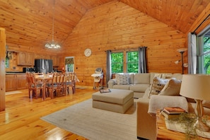 L’intérieur d’un chalet en bois comprend un coin repas, une cuisine, un salon et une grande fenêtre agrémentée de rideaux.
