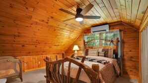 A cozy wooden cabin bedroom with a bed, a chair, a ceiling fan, and an air conditioning unit. - Unplug from the daily grind, whether a fun family getaway or a retreat with friends, this cabin is a perfect refuge to unwind and rejuvenate. Brand new Hot Tub! (Elliottsburg)