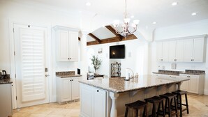 A spacious kitchen with white cabinetry, a large island with bar stools, and a chandelier.