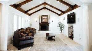 A spacious living room with a fireplace, a large sofa, and a television mounted on the wall.