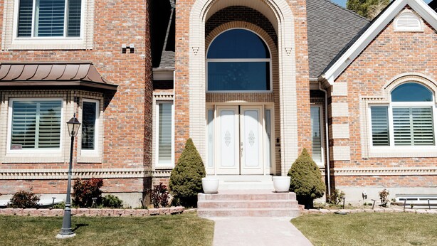A two-story brick house with a central entrance, a small porch, and a well-maintained lawn.
