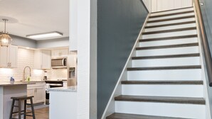 Een moderne keuken met witte kasten, een centraal eiland en een trap met donkere houten treden en witte wanden.