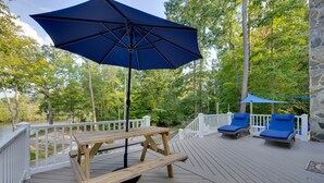 Um deck de madeira com mesa para piquenique e guarda-sol, cadeiras de lounge e um muro de pedra.