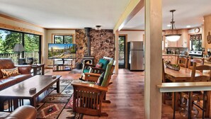 A cozy cabin interior with a stone fireplace, wooden furniture, a dining area, and a kitchen. - Forest Retreat - Hot Tub, Close to Lake (Carnelian Bay)