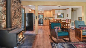 A cozy living room with a fireplace, wooden furniture, and a kitchen in the background. - Forest Retreat - Hot Tub, Close to Lake (Carnelian Bay)