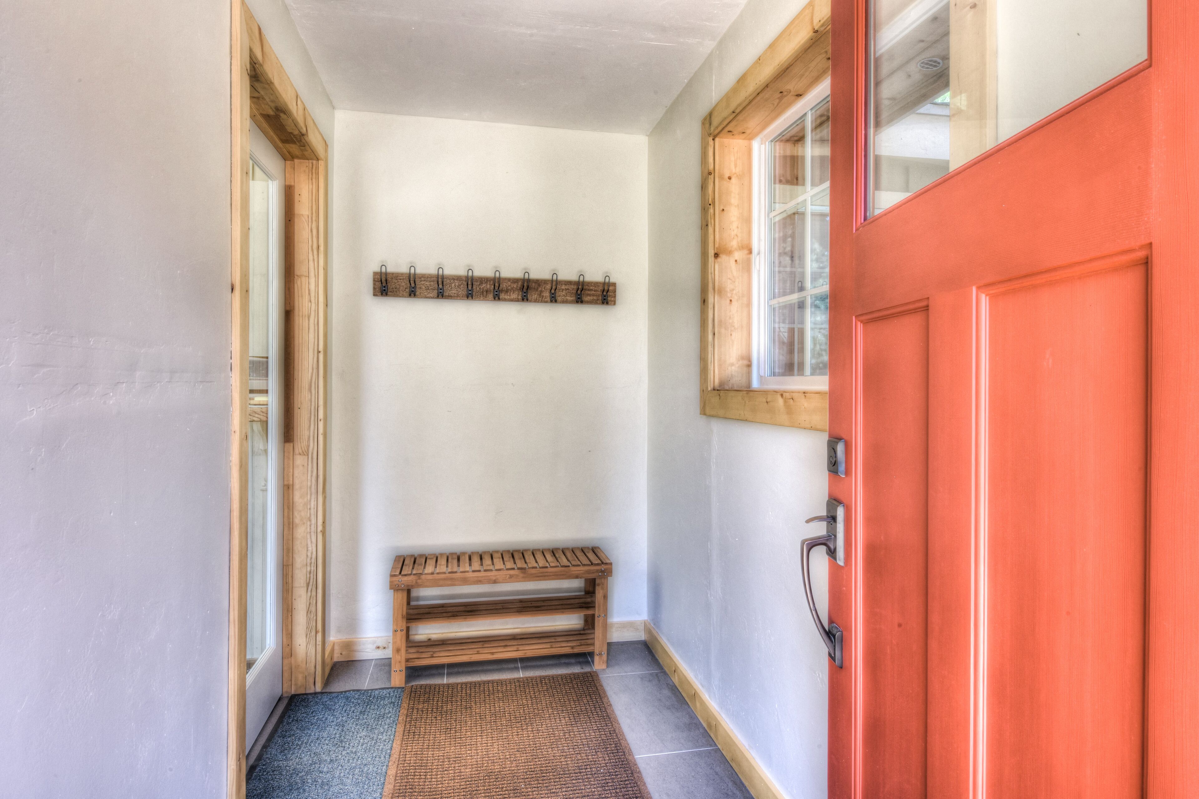 A hallway with a wooden bench, a red door, and a wall-mounted coat rack.