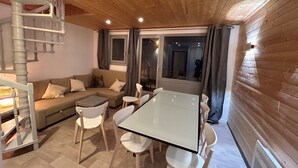 Un salon chaleureux avec un plafond en bois, un ensemble de canapés, une table à plateau en verre et un escalier en colimaçon.