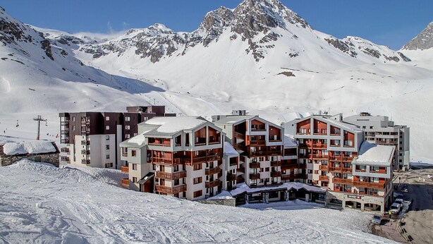 Une station de montagne enneigée, avec des bâtiments à plusieurs étages dotés de balcons et de pistes de ski.