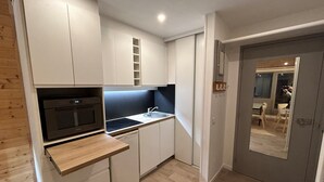 Une cuisine de taille réduite avec des meubles blancs, un four noir, un plan de travail en bois et un évier.