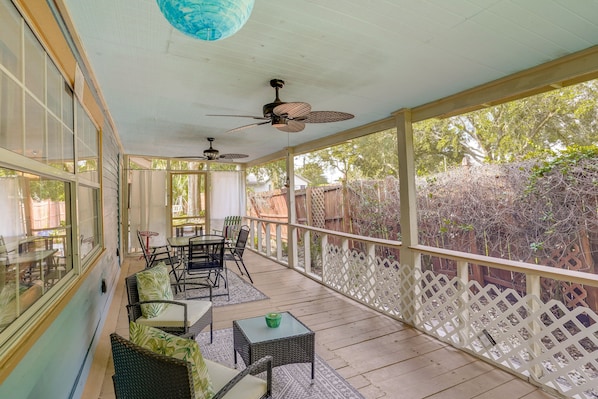Un patio techado con mobiliario de mimbre, ventiladores de techo y vista al jardín trasero.