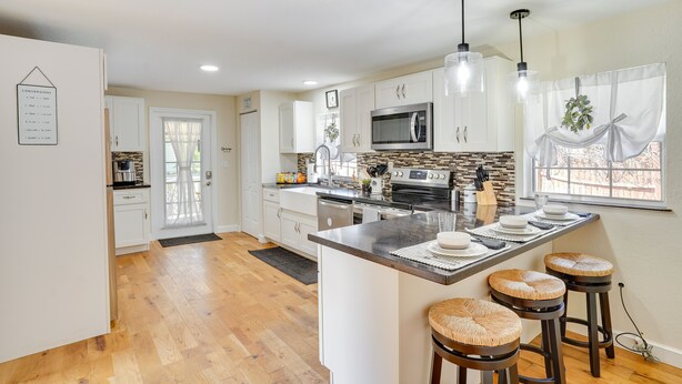 A modern kitchen with white cabinets, a central island with stools, a microwave, and a large window with curtains. - Lake Wales Vacation Rental w/ Screened-In Porch! (Lake Wales)