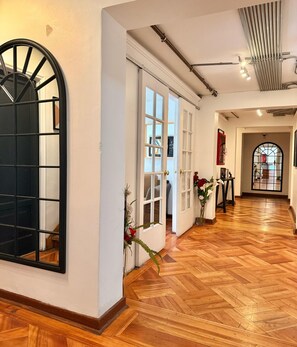 Un pasillo con suelo de madera, un gran ventanal arqueado y una puerta con diseño de rejilla.