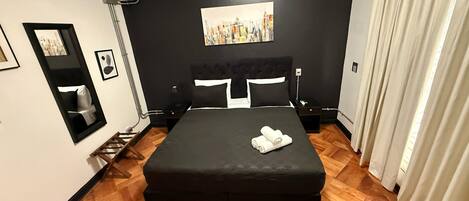 A hotel room with a large bed, a painting on the wall, a mirror, and a window with curtains.