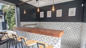Eine Bar mit einer Holztheke, Barhocker und Wandfliesen mit floralem Muster.
