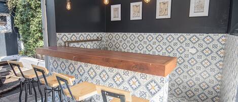Zona de bar con mostrador de madera, taburetes y paredes de azulejos con motivos florales.