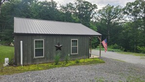 Une petite cabane en bois avec un toit en métal, deux fenêtres avec volets, une décoration en forme d’étoile et un drapeau américain.
