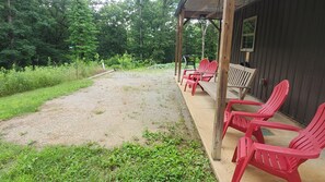 A covered porch with red plastic chairs, a concrete path, and a wooden building with a window.
