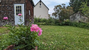 A rustic wooden house with a well-maintained garden featuring pink flowers and clover. - Sweet One Bedroom in the heart of the Keweenaw! (Ahmeek)