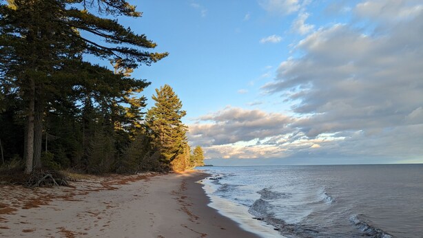 A beach with a sandy shore, trees, and a calm sea under a partly cloudy sky. - Sweet One Bedroom in the heart of the Keweenaw! (Ahmeek)
