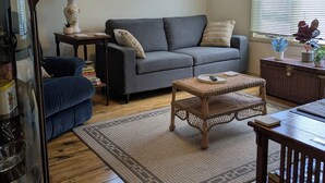 A living room with a grey sofa, blue armchair, wicker coffee table, and a large floor lamp. - Sweet One Bedroom in the heart of the Keweenaw! (Ahmeek)