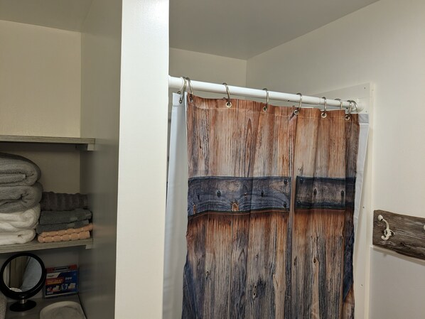 Un baño con cortina de madera, repisas con toallas dobladas y un botiquín.