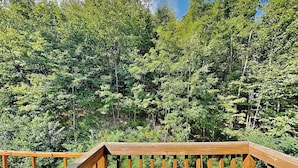 A wooden deck with a view of dense green forest. - Villages of Wisp 14 Winding Way by Taylor Made Deep Creek (McHenry)