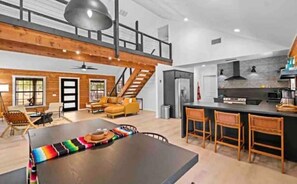 Relax in this spacious interior with a high ceiling and exposed beams, featuring a large table and comfortable seating for gatherings.