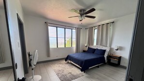 A bedroom with a bed, a ceiling fan, a nightstand, and a window with curtains. - Tropical Oasis 🇻🇮Stunning ocean view, minutes drive to Brewers Beach!🇻🇮🏝 (St Thomas)