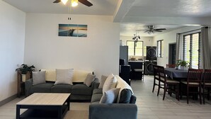 A living room with a sofa, coffee table, and a dining area with chairs and a table. There are ceiling fans and a painting on the wall. - Tropical Oasis 🇻🇮Stunning ocean view, minutes drive to Brewers Beach!🇻🇮🏝 (St Thomas)