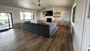 A spacious living area with a large gray sectional sofa, wooden flooring, a ceiling fan, and a fireplace. - New Custom Multi Master + Sleeping Room Golf Course Home w/ Outdoor Living Area  (Mattawa)